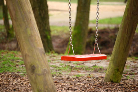A selective focus of a red swing in a garden surrounded by greenery under the sunlightの写真素材
