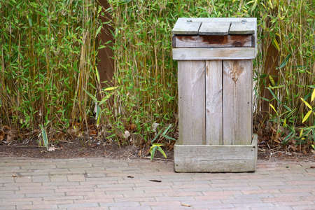 A wooden garbage bin near green plantsの写真素材