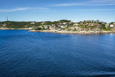 The sea surrounding Kristiansund covered in greenery and buildings under the sunlight in Norwayの写真素材