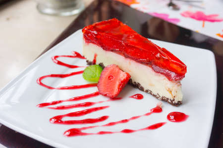 A closeup shot of a cheesecake covered with jelly and decorated with strawberry and a red jam