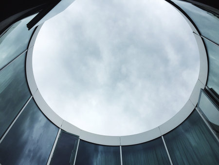 A low angle shot of the inside of a round building in a glass facade with a cloudy sky in the backgroundの写真素材