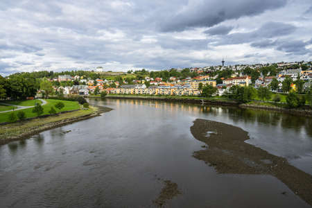 The Nidelva River surrounded by buildings and greenery under a cloudy sky in Trondheim in Norwayの写真素材