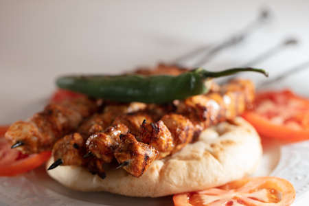 A selective focus shot of grilled meat on skewers on a pita bread with tomato slices and green...
