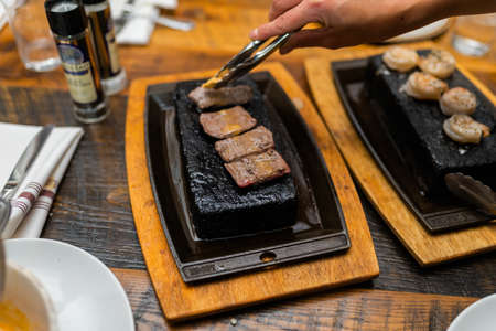 A selective focus shot of a person cooking meat on a hot stone with a blurred backgroundの写真素材