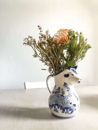 A vertical shot of a beautiful flower composition in a white vase on a white tableの写真素材