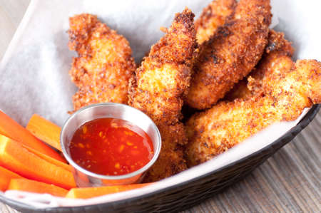 chicken tenders or strips with a spicy chilli sauce and vegetable sticksの写真素材