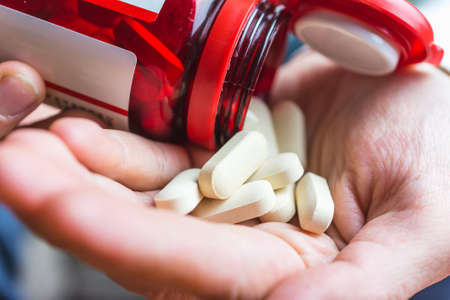 A person pouring white pills into his hand from a container