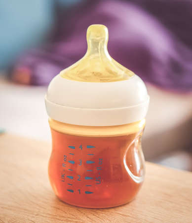 A closeup shot of a plastic bottle with a baby drink on a wooden surface with a blurred background
