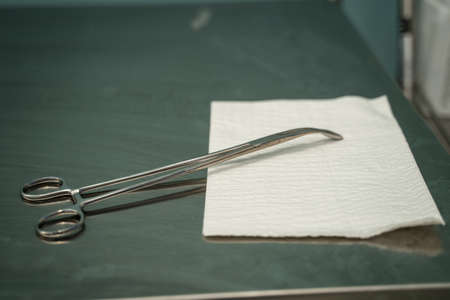 A closeup of a surgical scissor on a paper towel on the table under the lights