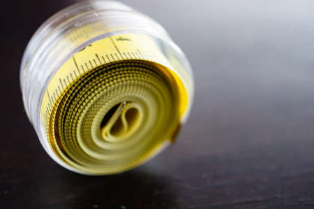 A close up shot of a rolled yellow measuring tape in centimeters on a wooden surfaceの写真素材