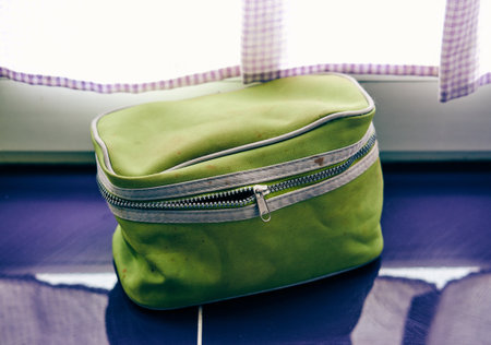 The green cosmetic bag near the window on a blue surfaceの写真素材