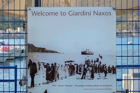A welcome sign with an old picture of passengers landing on the beach of Giardini Naxos, Italyのeditorial素材