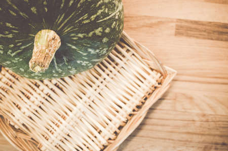 A high angle shot of a pumpkin and a basket on a wooden surfaceの写真素材