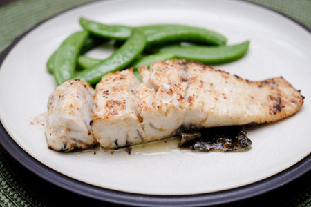 A piece of fried fish next to green vegetables on the plateの写真素材