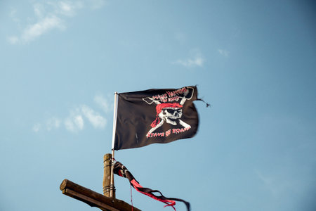 A low angle shot of a black pirate flag under a blue skyのeditorial素材