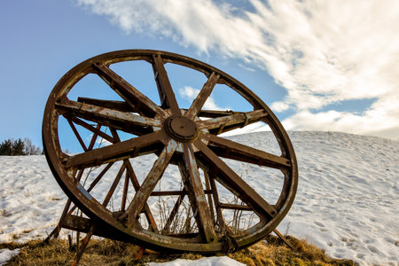 A low angle shot of a rusty metal cartwheel with a cloudy blue sky in the backgroundの写真素材