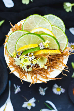 A raw vegan cake with lemon and lime on a black surface covered with tiny daisy flowers