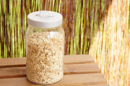 A glass jar filled with oat flakes on a wooden surface