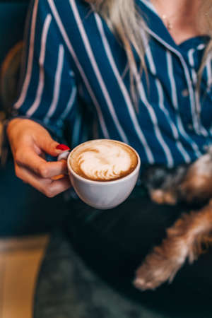 A high angle shot of a girl drinking caffe latte with her dog in a coffee shopの写真素材