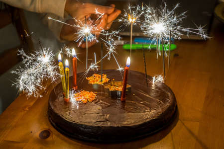 A selective focus shot of a delicious chocolate cake with sparkles and candles with a blurred...