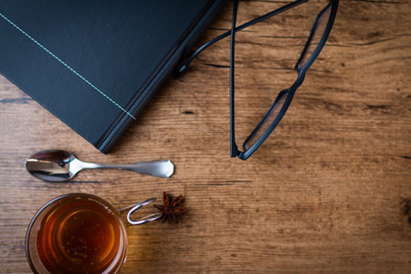 A top view of black notebook and eyeglasses with star anise tea and teaspoon on a wooden tableの写真素材