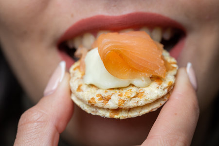 A closeup of a woman biting crackers with salmon and cream cheese under the lightsの写真素材