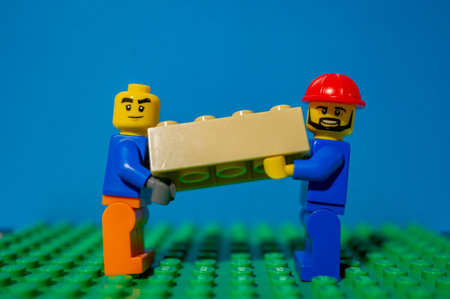 POZNAN, POLAND - Nov 20, 2020: Lego construction worker team carrying a heavy block together.のeditorial素材
