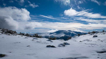 A landscape of rocky mountains covered in the snow under a cloudy sky in winter