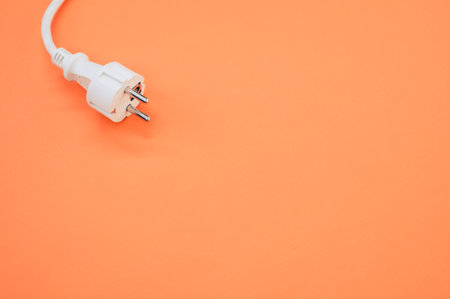 A high angle shot of an electrical wire and plug on an orange surface