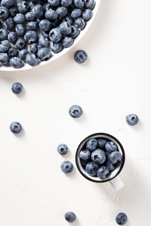 A top view shot of blueberries in a mug and on a white plate on  white surfaceの写真素材