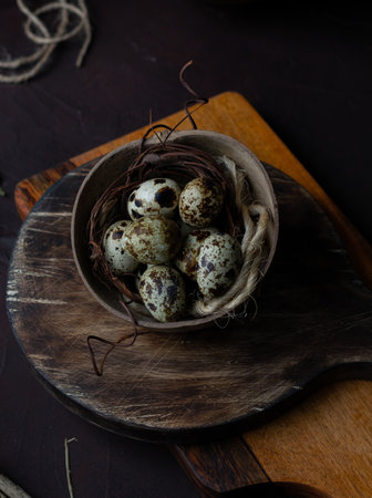 An overhead shot of speckled quail eggs with jute twine in a rustic bowl on a wooden boardの写真素材