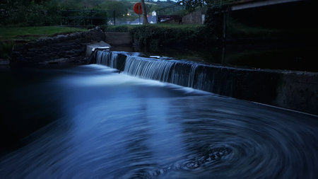 A high angle shot of a waterfall in a park with greenery on the background