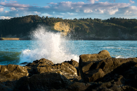 The beautiful shot of the waves of the sea crashing into the rock near the beach on a sunny dayの写真素材