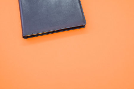 A top view closeup of a black notebook with a yellow bookmark isolated on an orange backgroundの写真素材