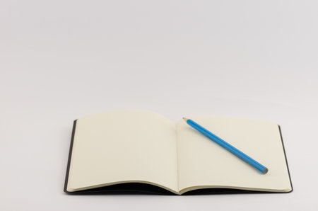 A closeup shot of an open blank book with blue colored pencil isolated on a white backgroundの写真素材