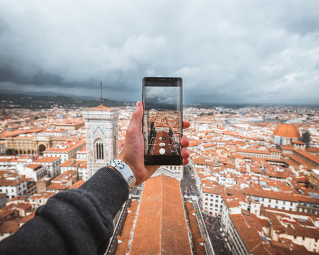 Human hand holding a smartphone to take a picture of Florence in portrait with cloudy sky from the top of the Domeのeditorial素材