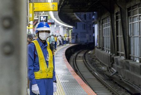 TOKYO, JAPAN - Jun 07, 2019: Photo of a JR staff member waiting for oncoming train at a railway...
