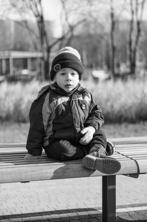 POZNAN, POLAND - Mar 22, 2020: Small two years old boy sitting on a bench at the Rataje park in black and white tones.のeditorial素材