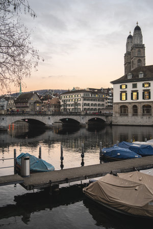 A vertical shot Zurich, Switzerland featuring the Grossmunster church steeple, Munsterbrucke bridge over Limmat river and dock with boatsのeditorial素材
