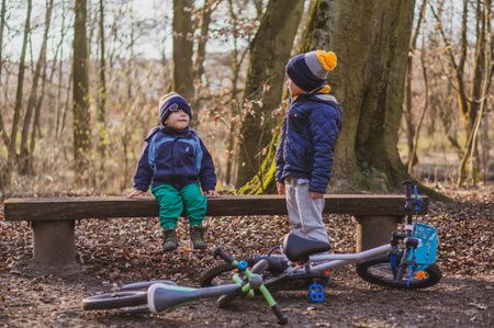 POZNAN, POLAND - Mar 14, 2020: Two boys resting by a wooden bench with bicycles in the Debiec forest.のeditorial素材