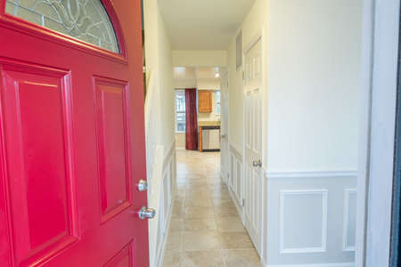 A beautiful shot of a red open door with white walls, doors and floor tiles inside the house