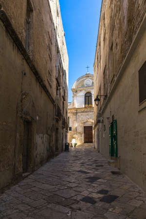 A vertical shot of a corridor between the old historic buildings in the Monopoli historic center, Apulia, Italyのeditorial素材