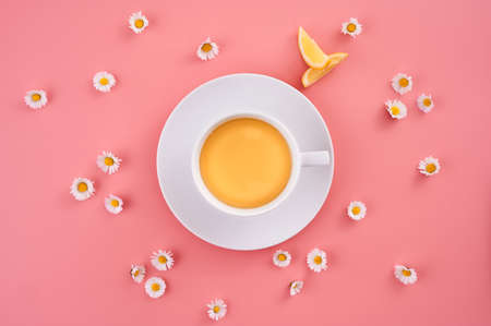 A high angle shot of a cup of orange juice surrounded by small daisy flowers on a pink surface