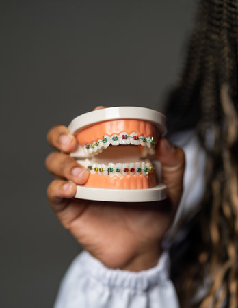 A vertical shot of a person holding prosthesis teeth with braces under the lightsの写真素材