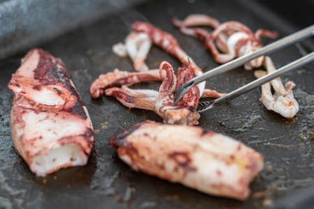 A closeup of a person frying small octopuses on a pan under the lights