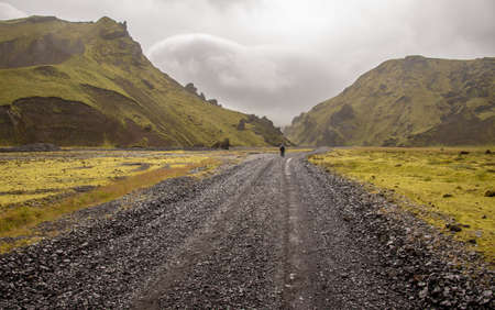 A road surrounded by hills covered in greenery under the sunlight and a cloudy sky