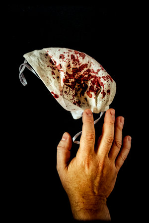 A closeup vertical shot of a man's hand touching a bloody face mask - the horror conceptの写真素材