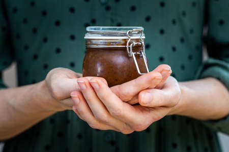 A closeup shot of female hands holding a homemade vegan raw plum jam in a glass jarの写真素材