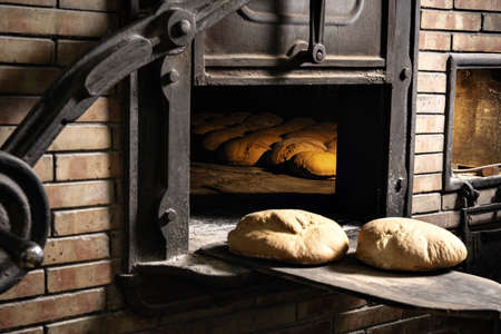 a closeup shot of two loaves of freshly baked bread being taken out of an old masonry brick ovenの写真素材