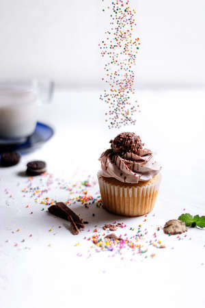 A vertical shot of a chocolate cupcake and sprinkles pouring from top